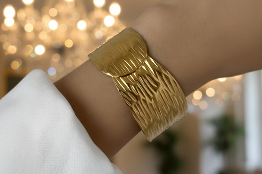 Gold bracelet on a wrist with a plain background