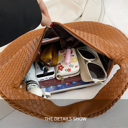 Brown woven handbag with various items inside, including a phone and sunglasses, on a light gray background.