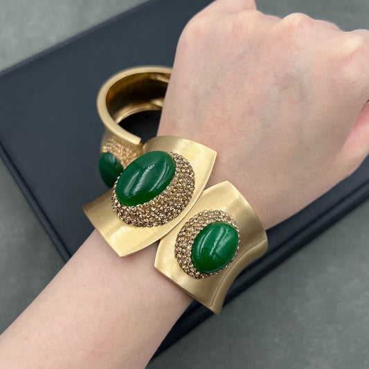 Gold bracelet with green stones on a wrist against a dark background