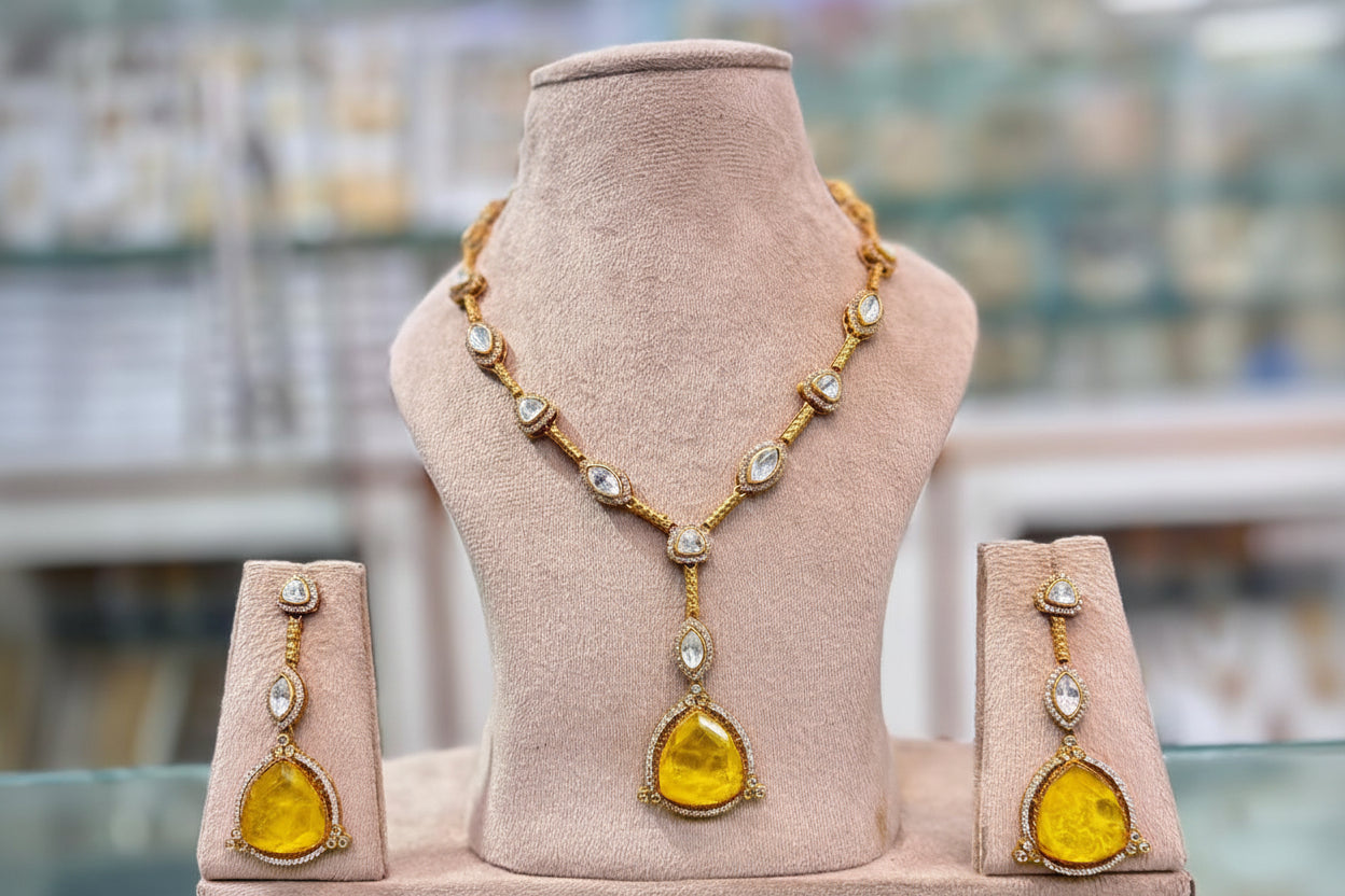 Gold necklace with yellow stones on a mannequin bust, accompanied by matching earrings, with a blurred background.