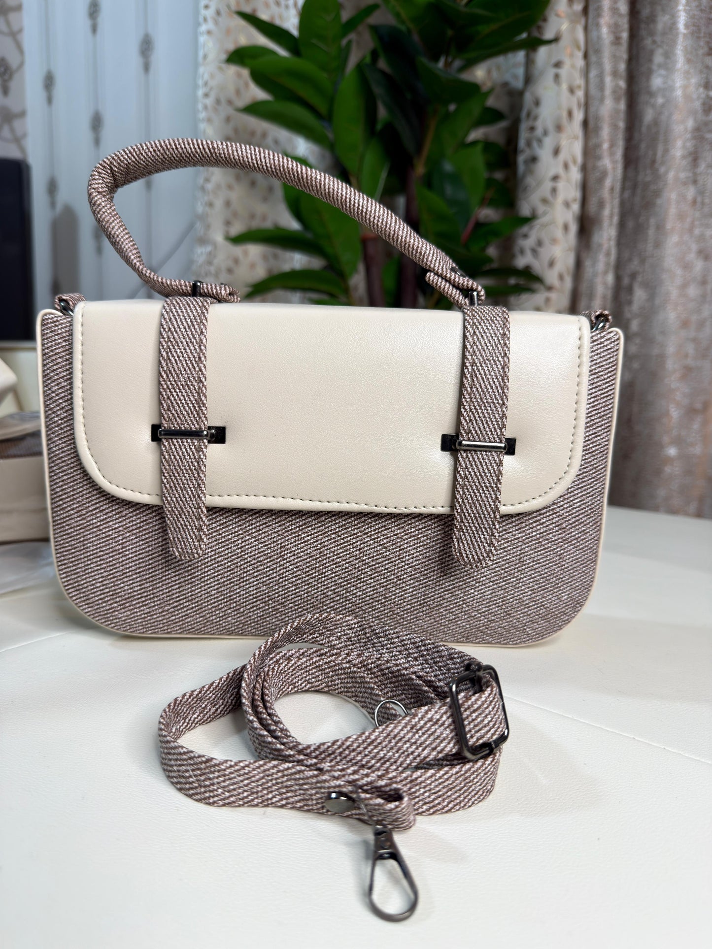 Two-tone handbag with a strap on a light surface with a plant in the background