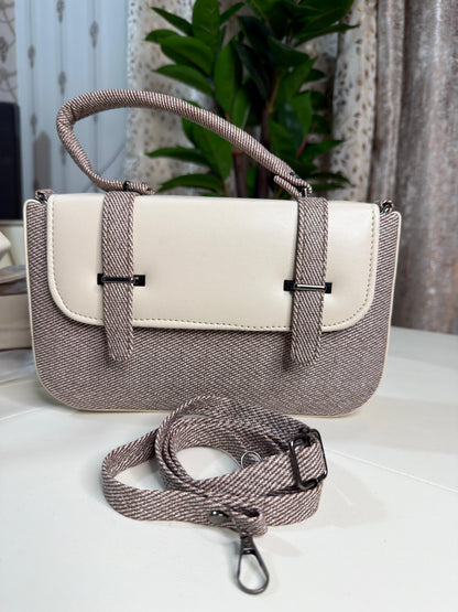 Two-tone handbag with a strap on a light surface with a plant in the background