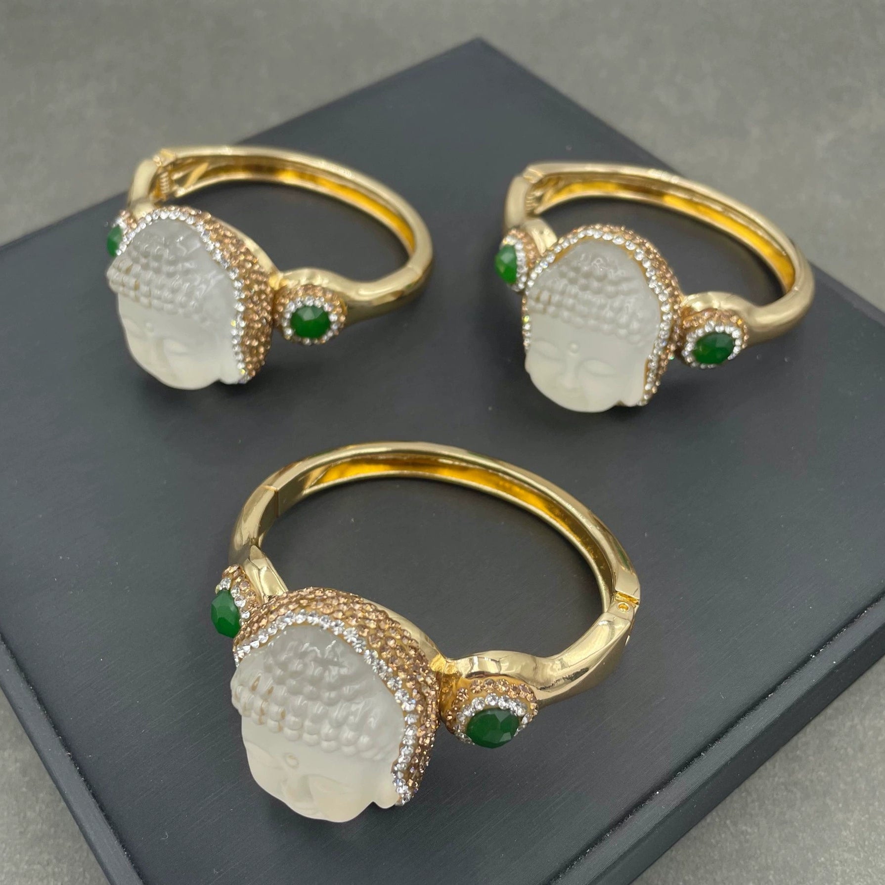 Three gold rings with green gemstones on a dark surface