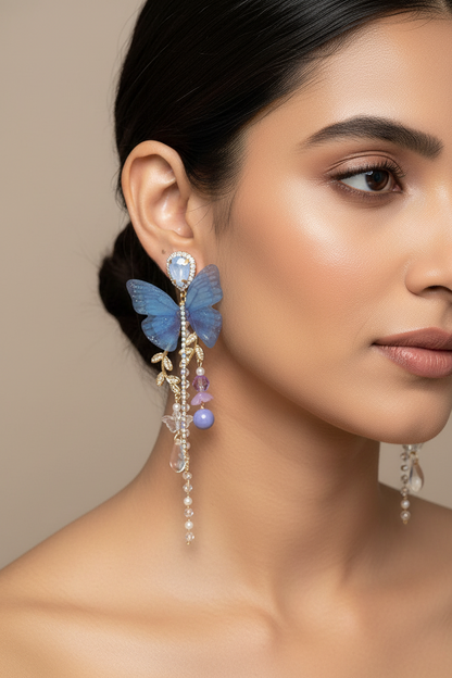 Butterfly-shaped earrings with beads held by a hand against a neutral background