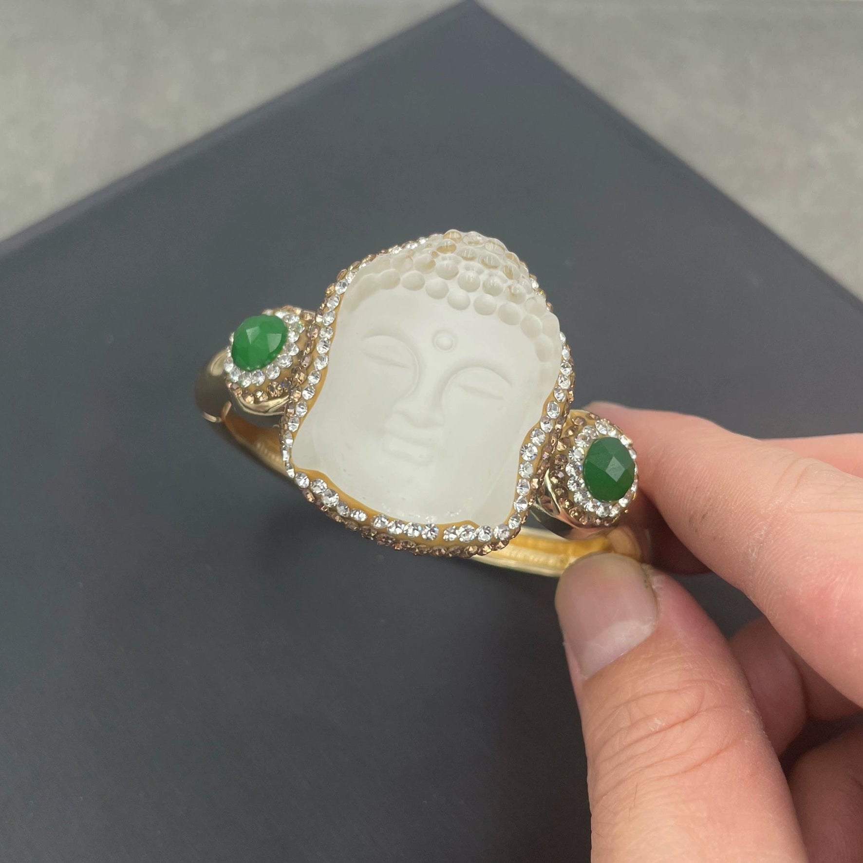Hand holding a jade ring with green gemstones on a dark surface