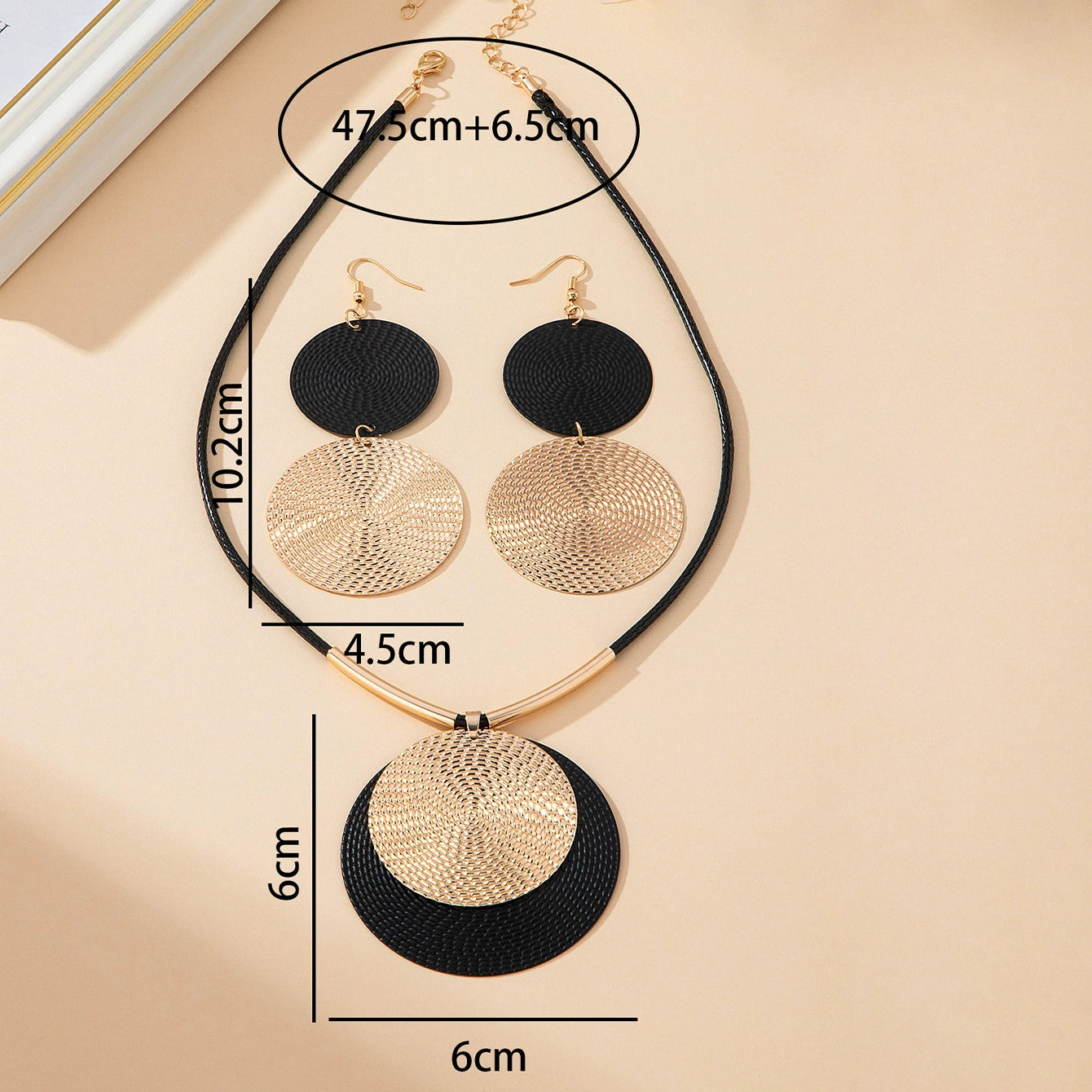 Necklace with black and gold circular pendants on a beige background, showing measurements.