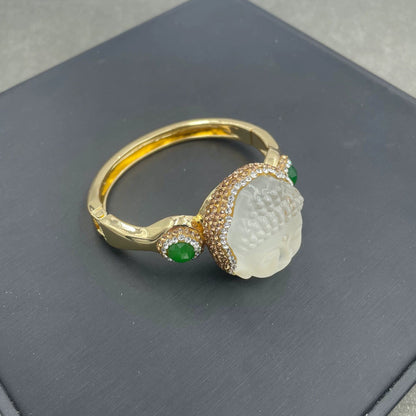 Gold ring with a white stone and green gemstones on a dark surface